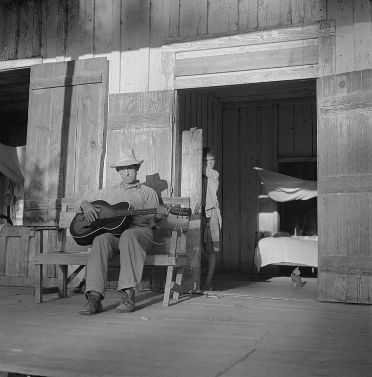 A farmer playing an archtop guitar on his porch in the evening, Louisiana, 1940